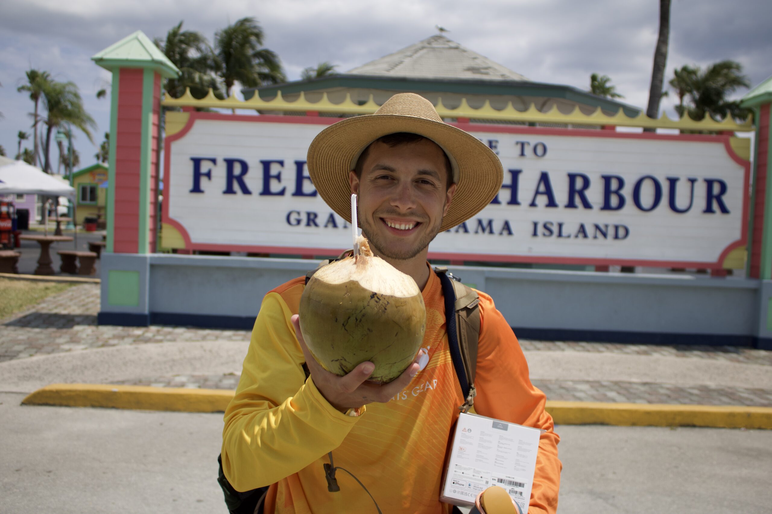 Dylan posing with a coconut drink in front of the Freeport Harbour sign in Grand Bahamas