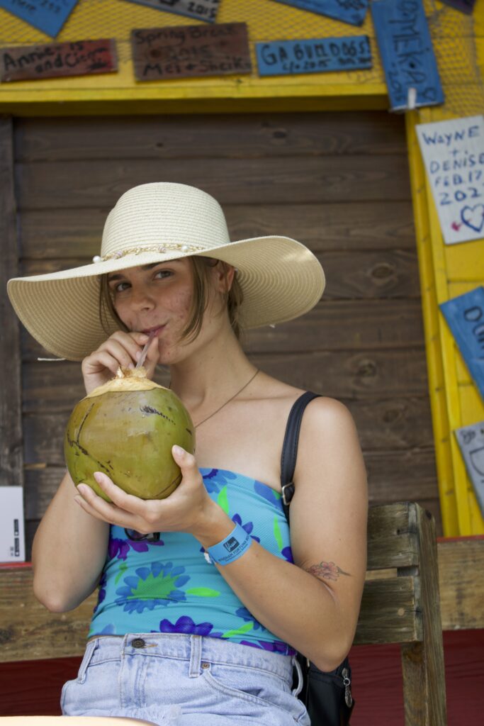 Sam drinking out of a coconut at a bar at the Freeport Harbour wearing a beach sunhat.